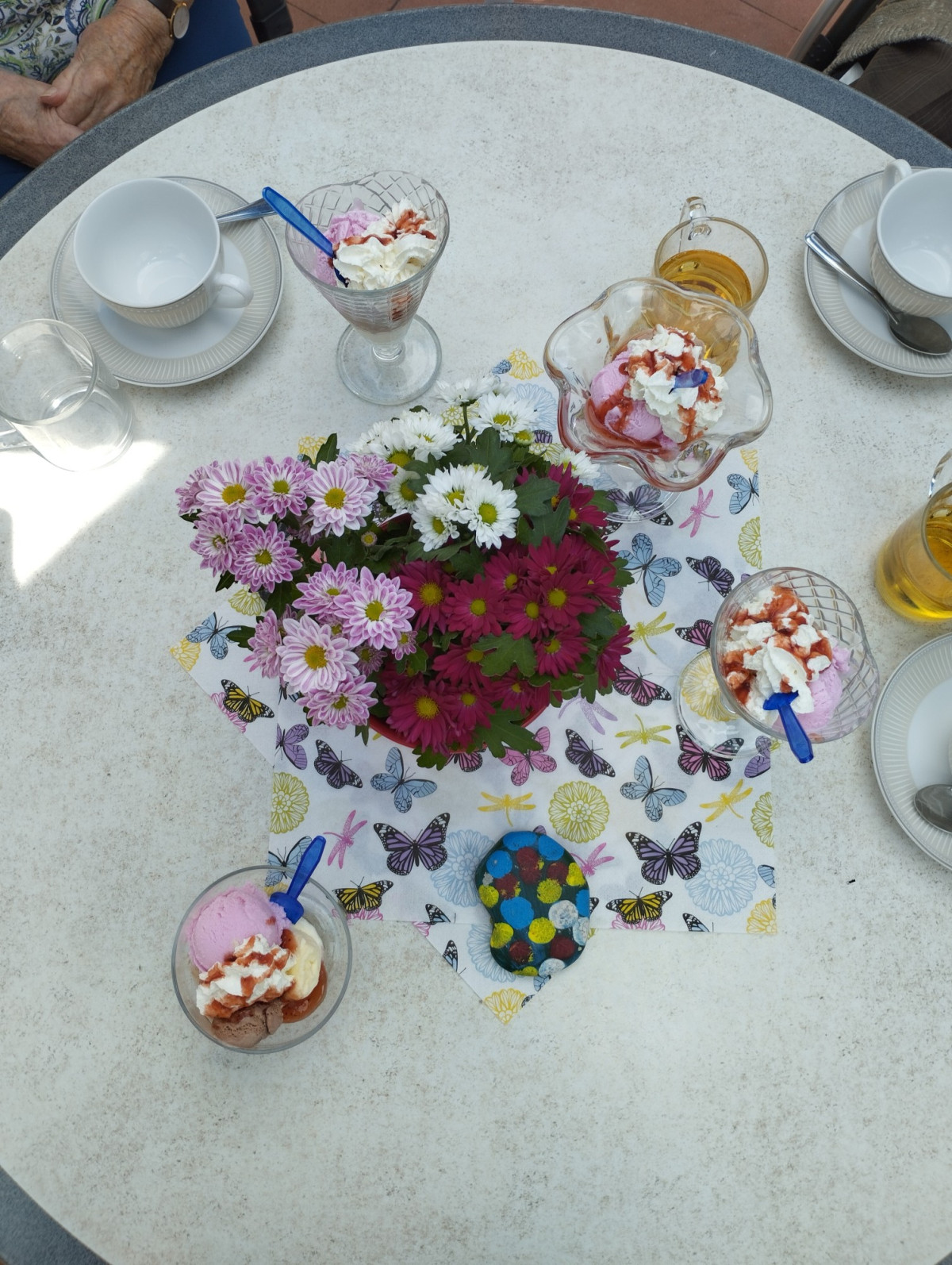 Bunter Blumenstrau&szlig; auf einem Tisch, umgeben von mehreren Eisbechern mit Sahne und Tassen.