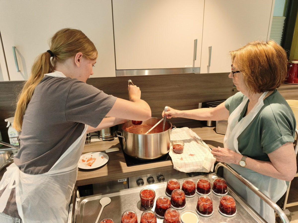 Zwei Frauen kochen gemeinsam Marmelade und f&uuml;llen sie in kleine Gl&auml;ser ab.