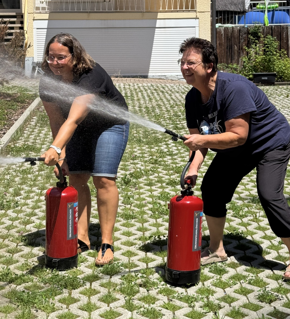 Zwei Frauen &uuml;ben den Umgang mit Feuerl&ouml;schern und richten die L&ouml;schstrahlen nebeneinander auf den Boden.