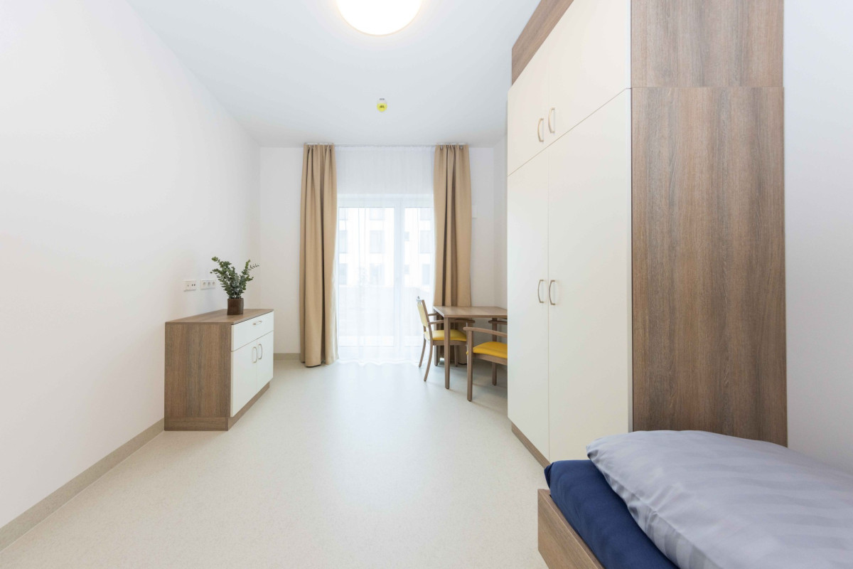 Helles Einzelzimmer mit Bett und Schreibtisch.