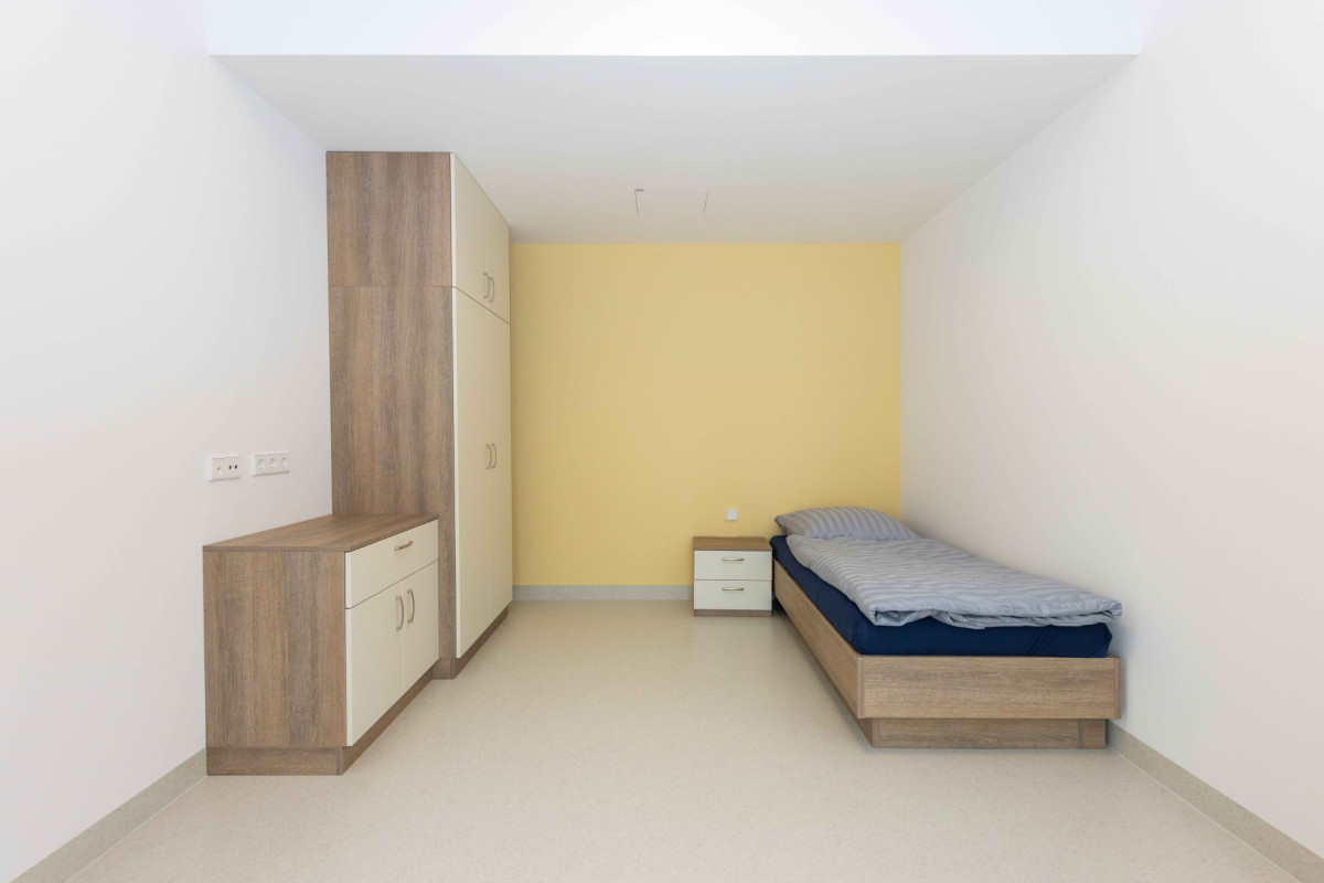 Schlafzimmer mit Bett, Schrank und gelbem Wandanstrich.