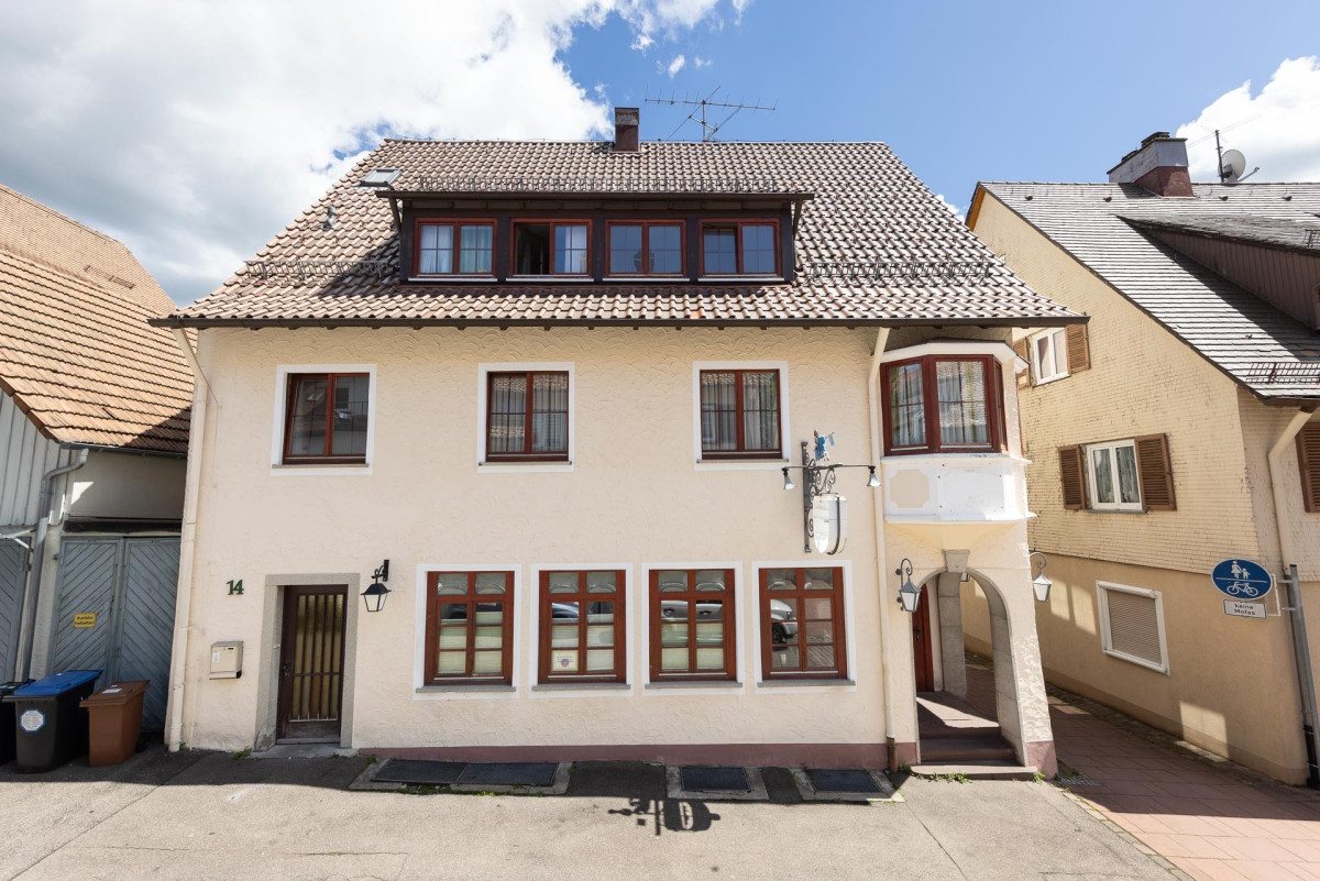 Wohnhaus mit Mansardendach und roten Fensterrahmen.