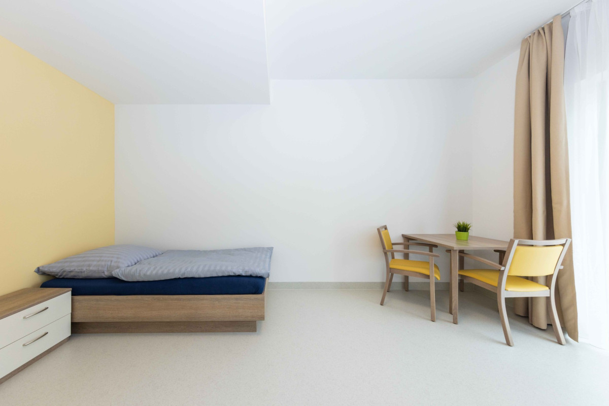 Helles Schlafzimmer mit Bett, Schreibtisch und Stuhl.