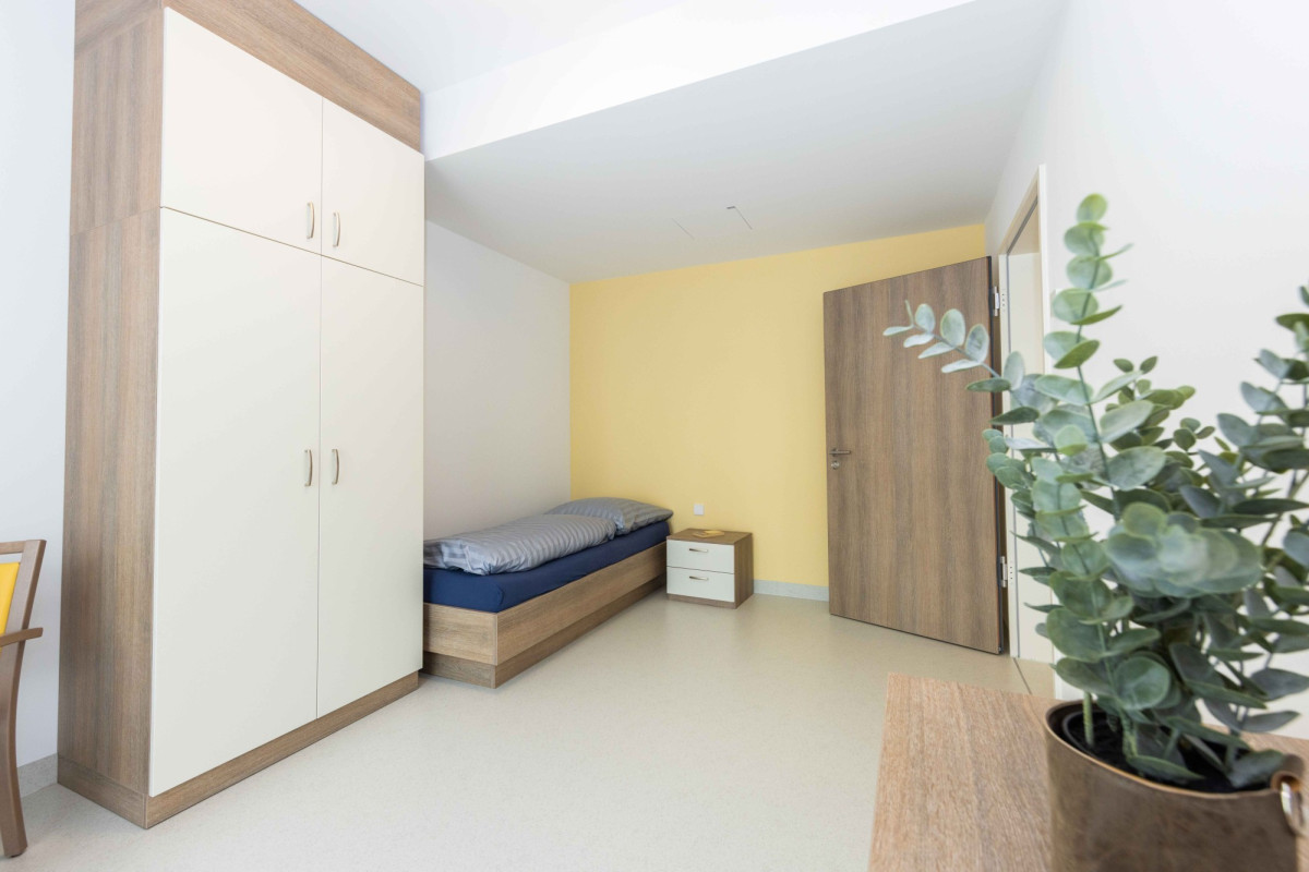 Helles Schlafzimmer mit Bett, Schrank und Pflanzen.