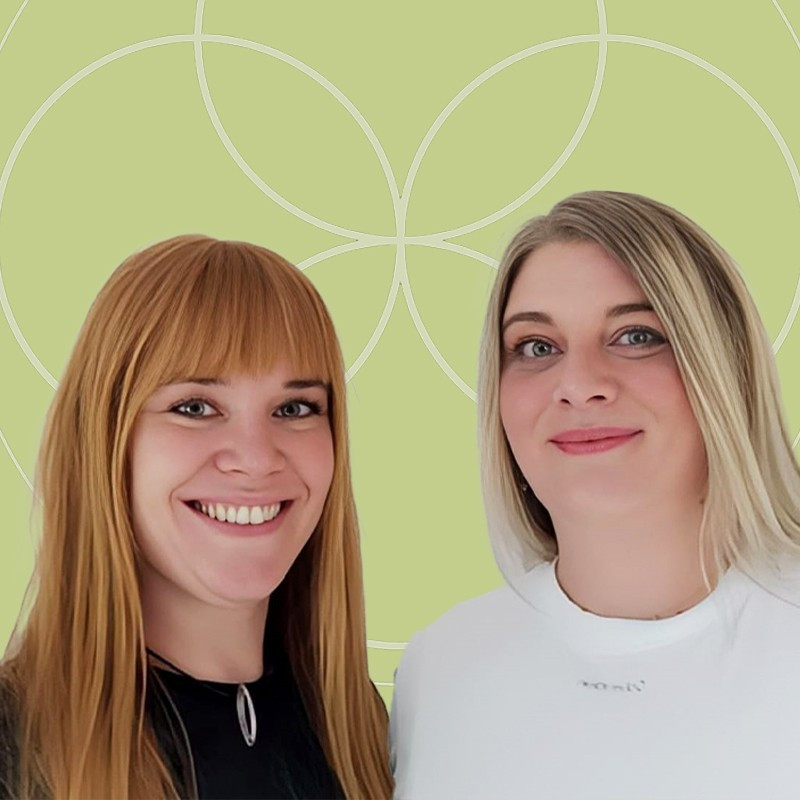 Zwei Frauen l&auml;cheln vor gr&uuml;nem Hintergrund.