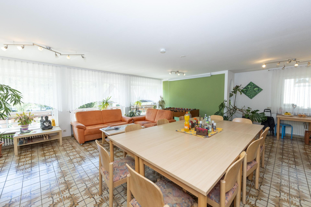 Heller Gemeinschaftsraum mit Holztisch und gr&uuml;ner Wand.