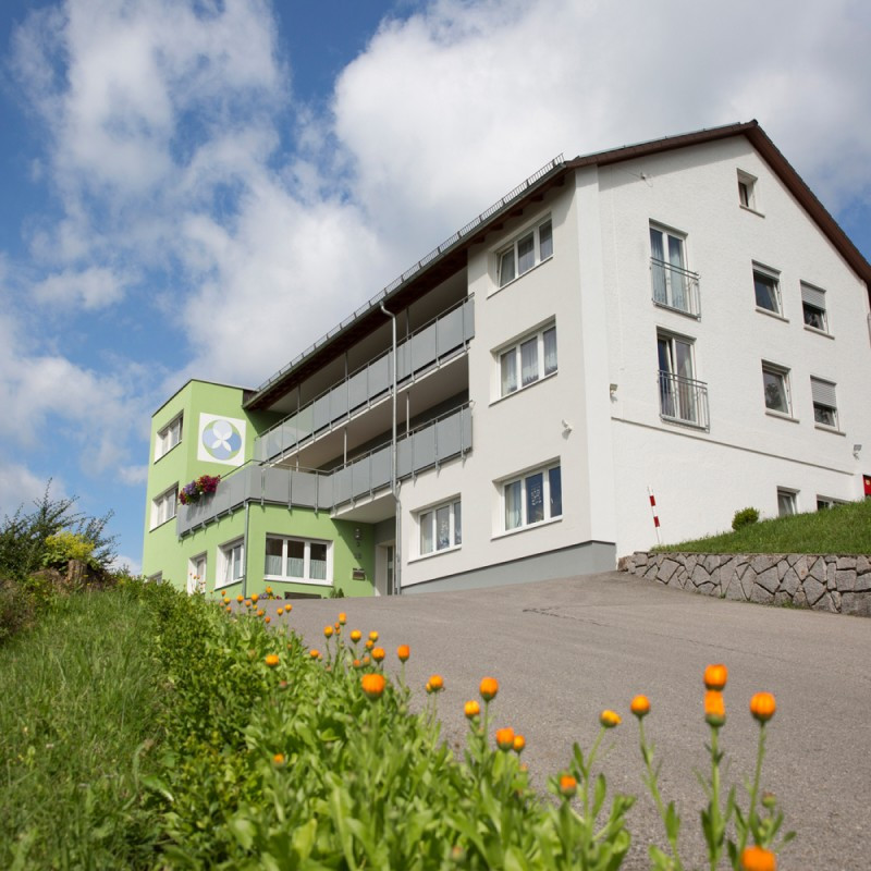Haus Berghof mit gr&uuml;nem Eingangsbereich und Wiese.