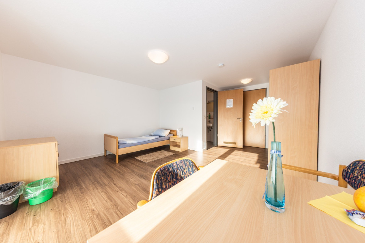 Helles Zimmer mit Bett, Tisch und Holzboden.