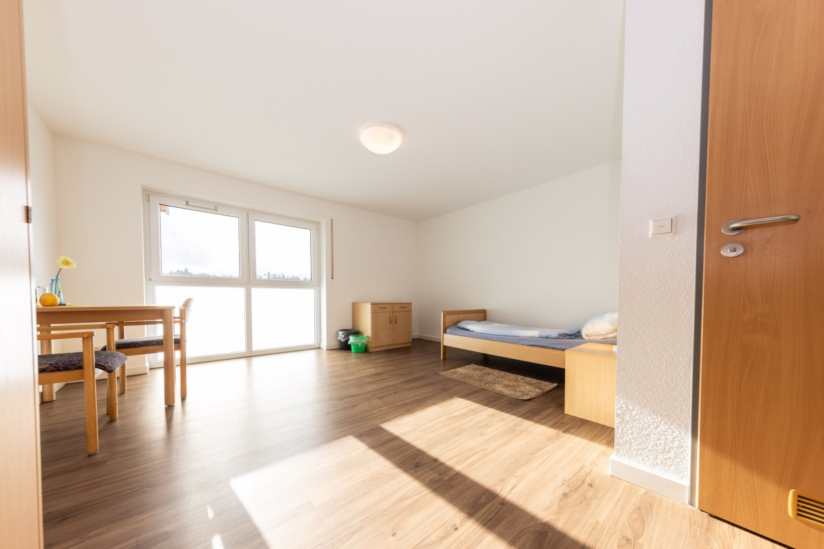 Helles Zimmer mit Bett, Tisch und gro&szlig;em Fenster.