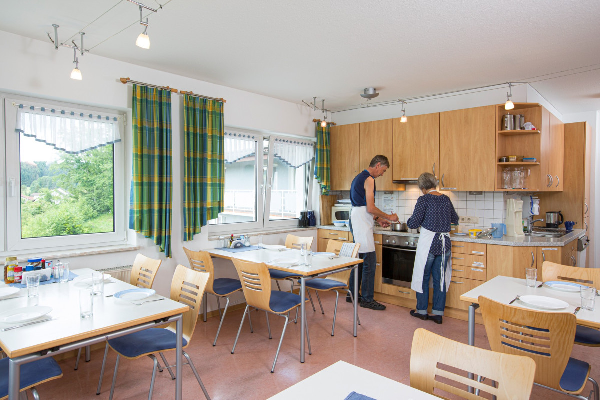 Gemeinschaftsk&uuml;che mit Holzm&ouml;beln und zwei Personen beim Kochen.
