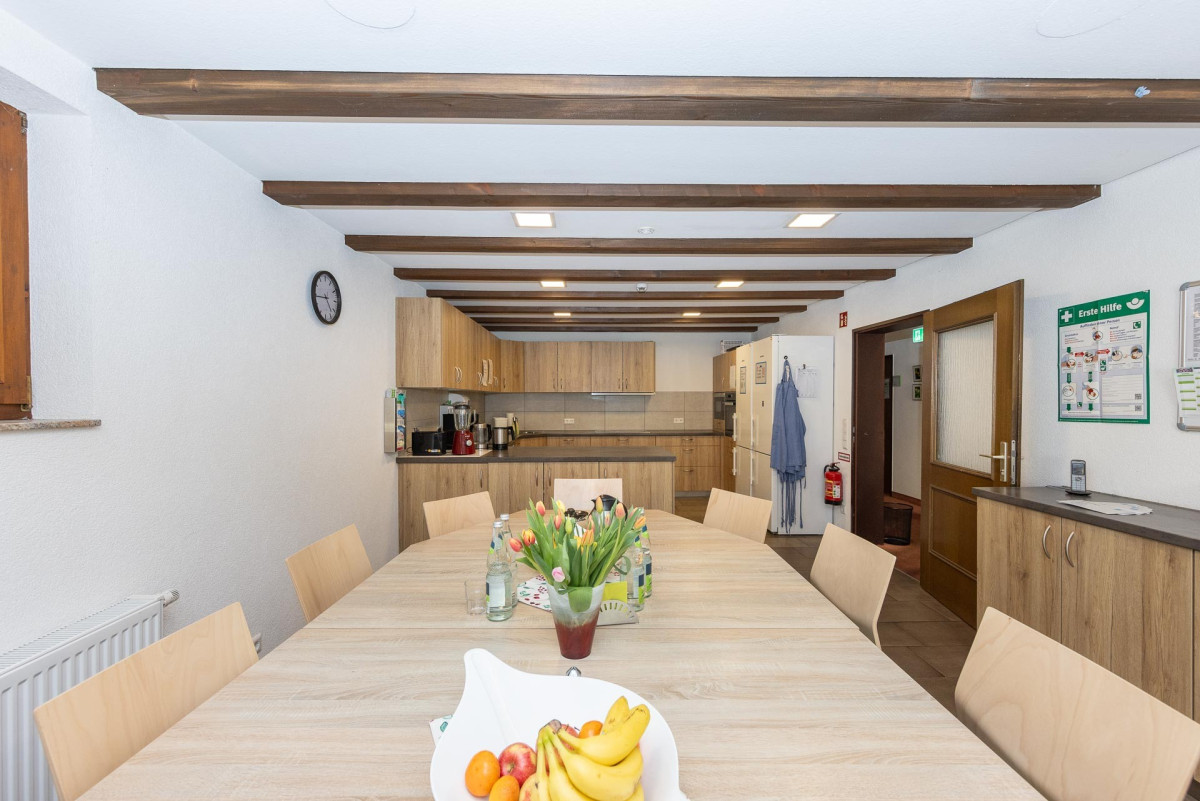 Helles Gemeinschaftszimmer mit Holzbalken und langem Tisch.