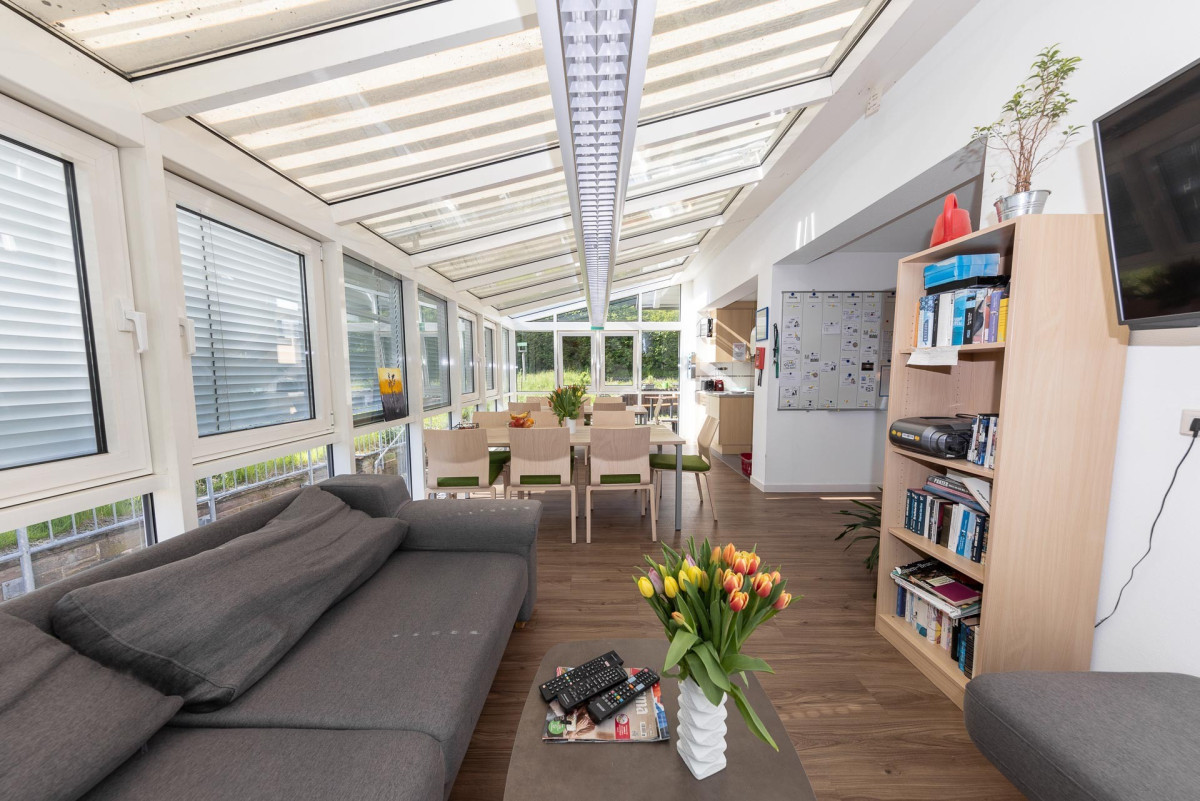 Moderner Wintergarten mit Sofa, Esstisch und gro&szlig;z&uuml;giger Verglasung.