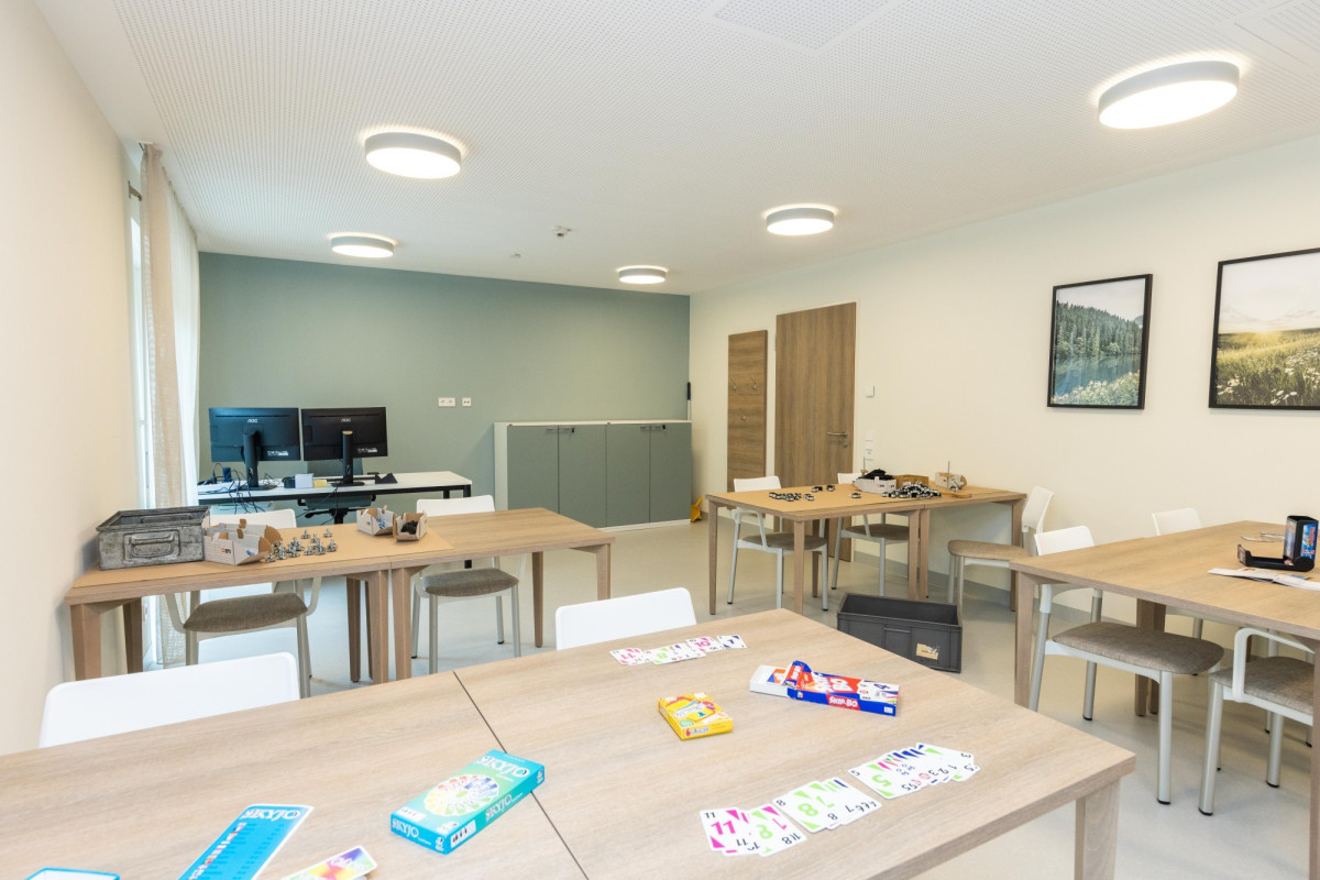 Helles Therapiezimmer mit Holztischen und Spielmaterialien.