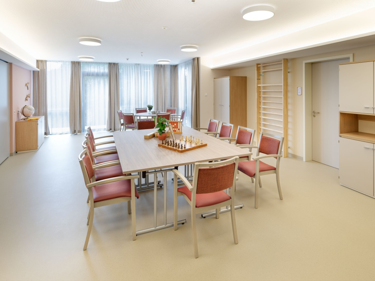 Heller Gemeinschaftsraum mit Tisch und roten St&uuml;hlen.